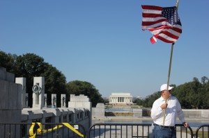 William Szych, of Alexandria, Va., holds an American flag in front of the barriers surrounding the Memorial. Behind him the fountains of the World War II and the Lincoln memorials sit dormant as a result of the government shutdown. 