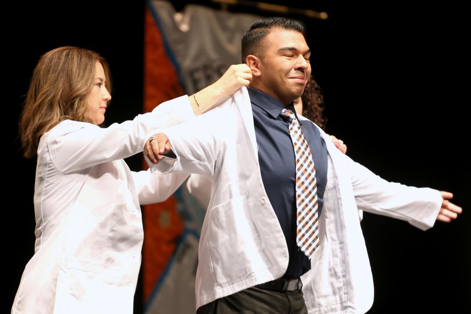 Director of experiential education clinical professor Jacquelyn P. Navarrete and chair of pharmacy practice and clinical sciences clinical professor Amanda M. Loya help students put on coats during the presentation of white coats.
