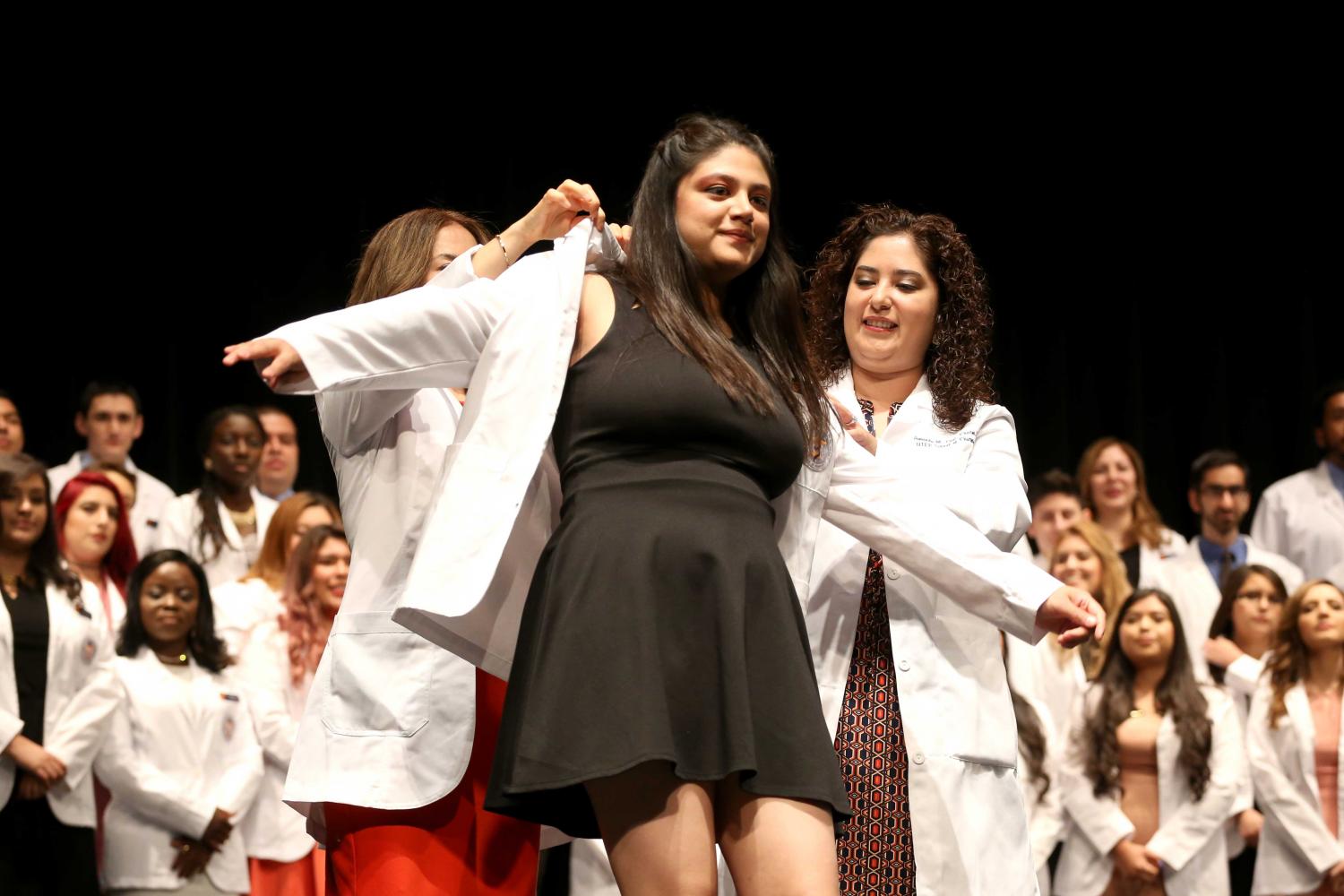 Director of experiential education clinical professor Jacquelyn P. Navarrete and chair of pharmacy practice and clinical sciences clinical professor Amanda M. Loya help students put on coats during the presentation of white coats.