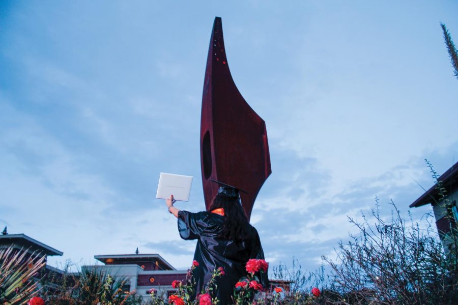 A UTEP student takes their senior graduation picture in front of the pick located at the front of the UTEP campus.