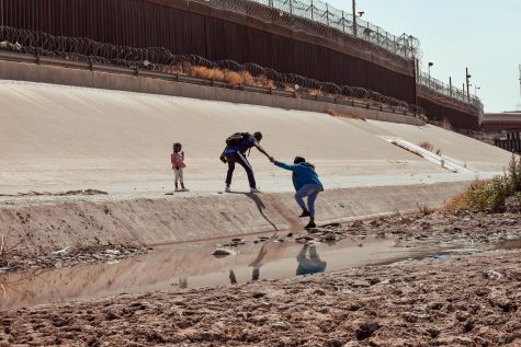 An immigrant from Haiti helps a woman climb concrete to cross the United States border seeking asylum. 