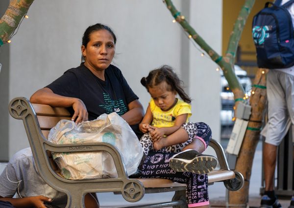 A mother with her daughter sitting nearby El Paso Street with their belongings. 