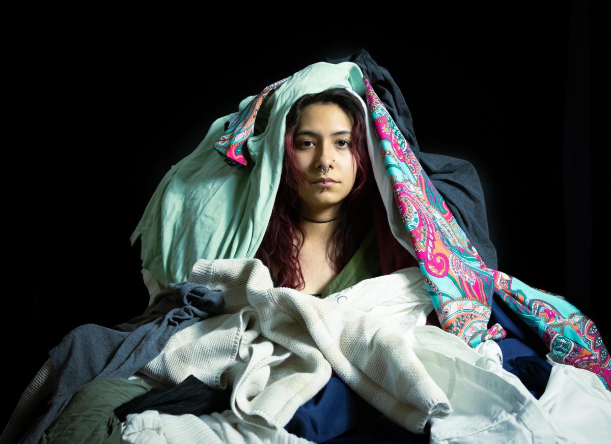 Amaris Juarez peers through layers of thrifted clothes, portraying the challenge of finding authenticity in thrift stores in the age of fast fashion.