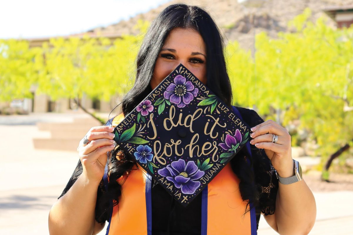 A UTEP graduate holds up a custom cap honoring loved ones, highlighting the tradition of personalized messages at graduation.