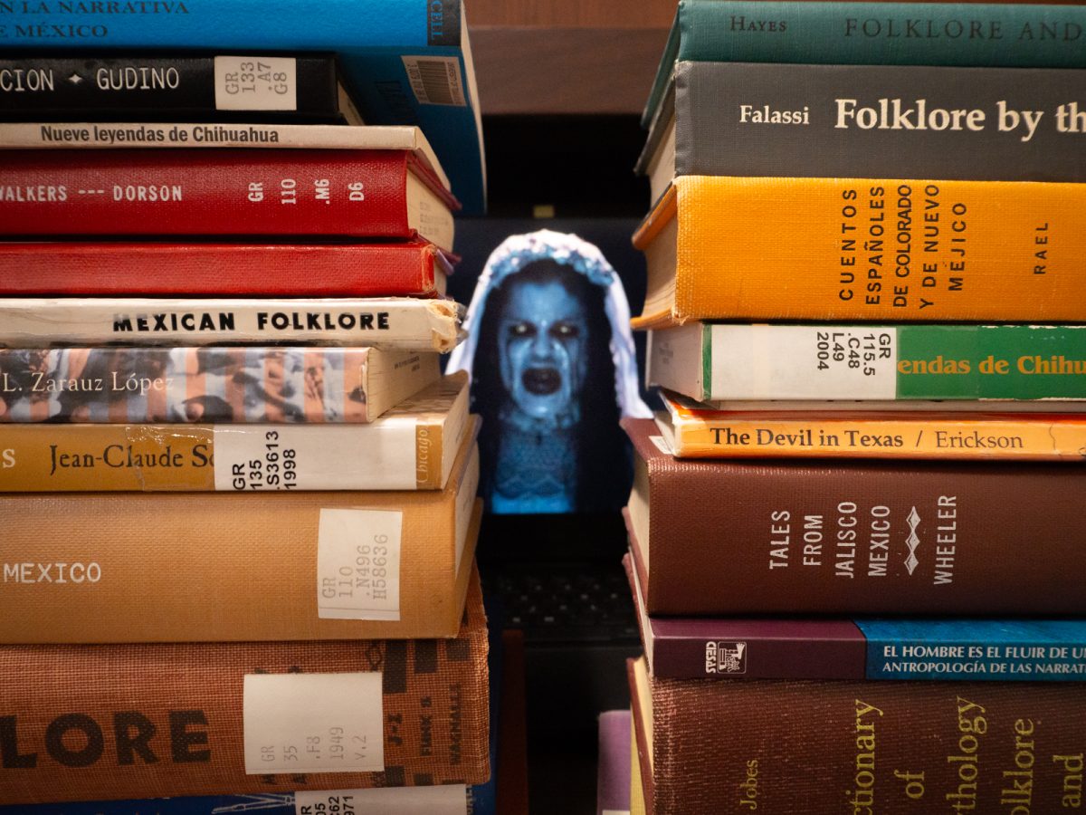 An image of “La Llorona” (© Warner Bros. Pictures) visible through stacks of Mexican and Mexican-related folklore books.