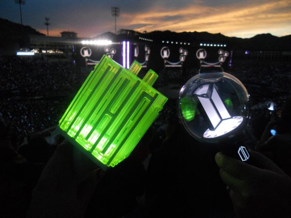 A neon green NCT light stick glows beside an official BTS light stick in the crowd.
